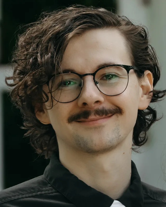 Ross Adolphi, smiling, in glasses and a dark shirt